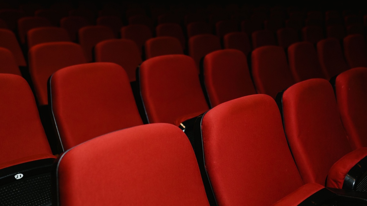 Rows of red upholstered seats inside a dimly lit movie theater.